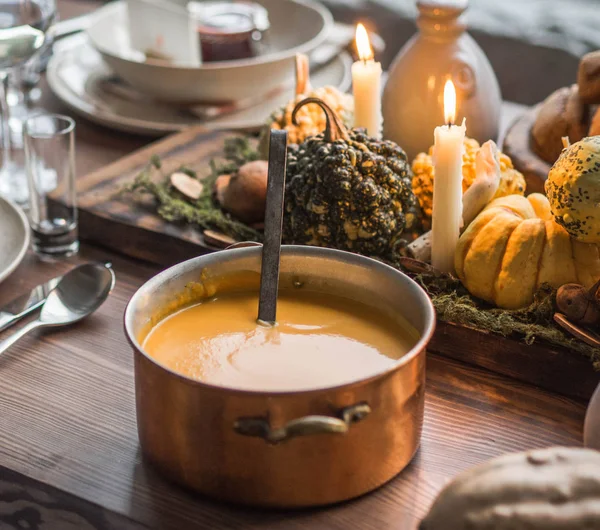 Table setting for Thanksgiving. Autumn table with pumpkins and candles. Big cooper pan with orange pumpkin soup.