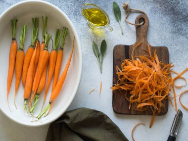 Genç bir beyaz oval seramik tavada, pişmiş hazır portakal havuç ve bir polis yanındaki ahşap bir gemide temizlenmiş havuç soyulmuş. Üstten görünüm