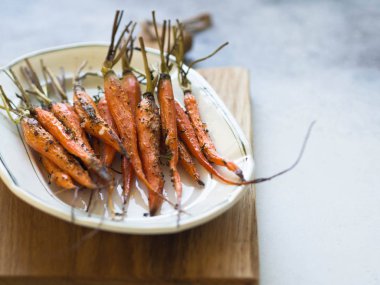 Ahşap tahta üzerinde beyaz oval plaka üzerinde genç turuncu havuç pişmiş. Kopya alanı