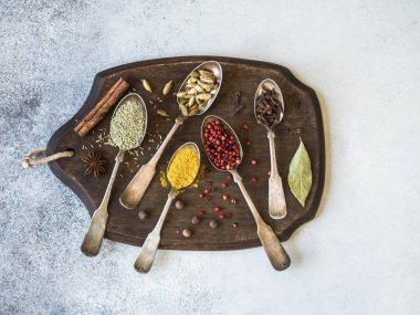 Koyu ahşap tahta üzerinde vintage kaşık içinde çeşitli baharatlar. Kuru otlar, gri bir arka plan üzerine tuz baharat. Üstten görünüm