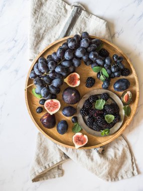 Mor meyve, çilek ve yeşil nane yaprakları. Böğürtlen, üzüm, Erik ve beyaz mermer zemin üzerinde bir ahşap tepsi incir. Olgun ve lezzetli meyve ve çilek.