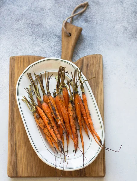 Baked young orange carrots on white oval plate on wooden board.