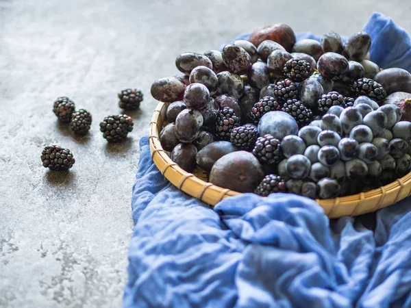 Purple fruits and berries. Blackberries, grapes, plums and figs in a wooden tray on dark background. Tasty and ripe fruits and berries.