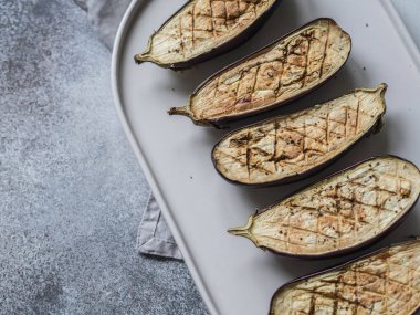 fırında patlıcan dilimleri ile tuz, baharat ve otlar bir oval beyaz seramik plaka üzerinde gri bir arka plan üzerinde.