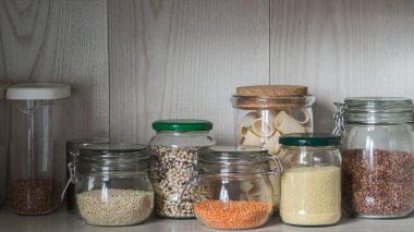 Raf tahıl çeşitli kavanoz ile mutfakta. Makarna, mercimek, kuskus, fasulye, quinoa ve buğday bir kap ile cam kavanoz.