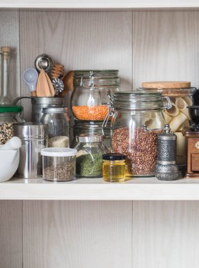 Raf hububat ve mutfak araçları çeşitli kavanoz ile mutfakta. Makarna, mercimek, kuskus, fasulye ve quinoa ile cam kavanozlar. Kahve Öğütücü, tatlım, baharatlar, bitkiler, susam