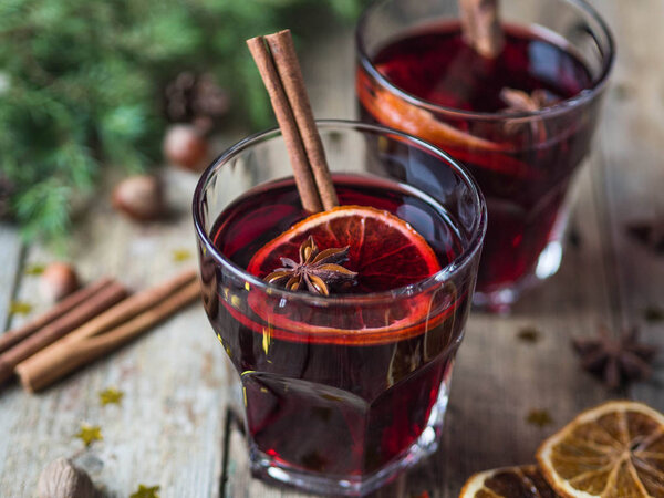 Traditional winter alcoholic drink - mulled wine. Hot wine with fruits and spices in glasses on old wooden background.