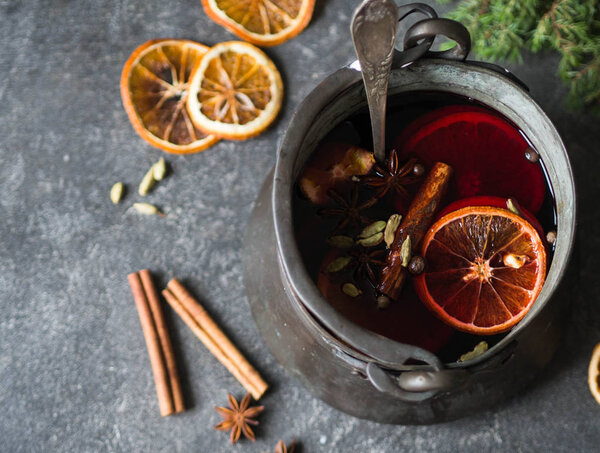 Traditional winter warming alcoholic drink - mulled wine. Hot wine with fruits and spices in vintage metal bowler on dark gray background.