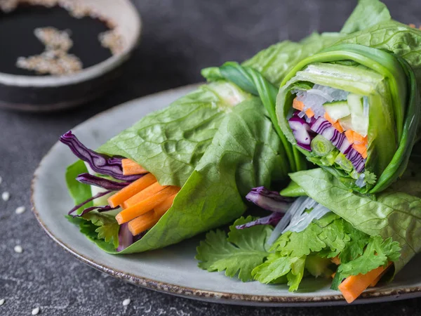 Rolls from lettuce leaf with vegetables and rice noodles and soy sauce with sesame. Vegetarian and vegan rolls with lettuce, carrots, red cabbage, rice noodles, cucumber