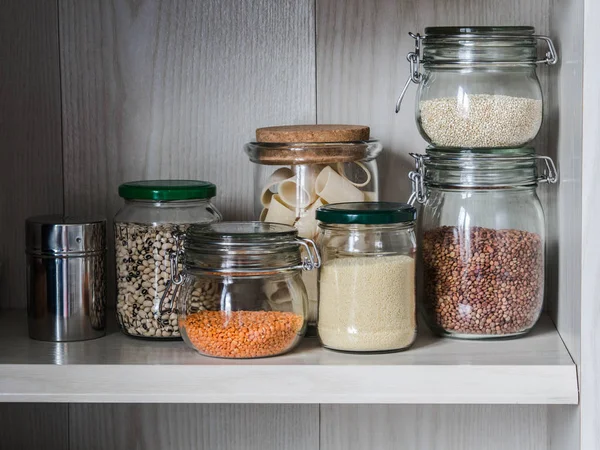 Police v kuchyni s různými sklenice obilovin. Sklenice s těstoviny, kuskus, čočka, fazole — Stock fotografie