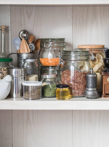 Shelf in the kitchen with various jars of cereals and kitchen tools. Glass jars with pasta, lentils, couscous, beans and quinoa. Coffee grinder, honey, spices, herbs, sesame