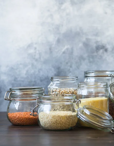 Açık gözlük kavanoz makarna, mercimek, kuskus, fasulye ve kahverengi ahşap masa üzerinde quinoa ile. — Stok fotoğraf