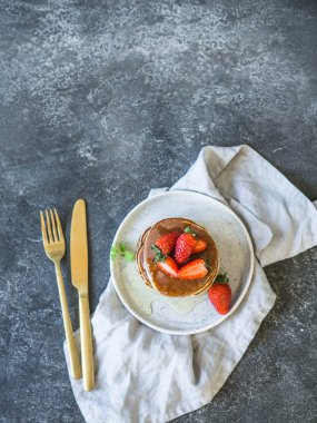 Bal ve gri bir tablo üzerinde beyaz bir plaka üzerinde çilek ile krep yığını. Üstten görünüm