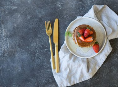 Bal ve gri bir tablo üzerinde beyaz bir plaka üzerinde çilek ile krep yığını. Üstten görünüm