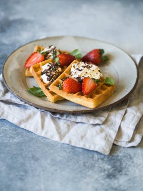 Krema, çikolata ve çilek rustik gri bir arka plan üzerinde gri bir tabakta ile Belçika Waffle.