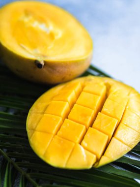 Gri arkaplanda palmiye yaprakları üzerinde olgun sarı mango dilimi.