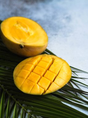 Gri arkaplanda palmiye yaprakları üzerinde olgun sarı mango dilimi.