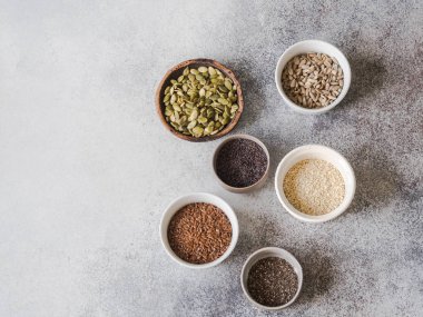 Çeşitli tohum - susam, keten tohumu, ayçiçeği çekirdeği, kabak çekirdeği, haşhaş, chia kase gri bir arka plan üzerinde. Kopya alanı.