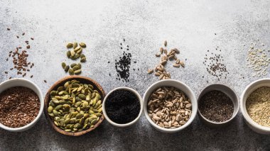 Çeşitli tohum - susam, keten tohumu, ayçiçeği çekirdeği, kabak çekirdeği, haşhaş, gri bir arka plan üzerinde kaseler chia.