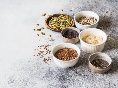 Çeşitli tohum - susam, keten tohumu, ayçiçeği çekirdeği, kabak çekirdeği, haşhaş, chia kase gri bir arka plan üzerinde. Kopya alanı.