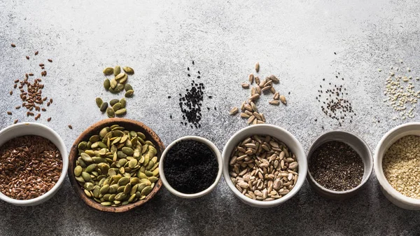 Çeşitli tohum - susam, keten tohumu, ayçiçeği çekirdeği, kabak çekirdeği, haşhaş, gri bir arka plan üzerinde kaseler chia.