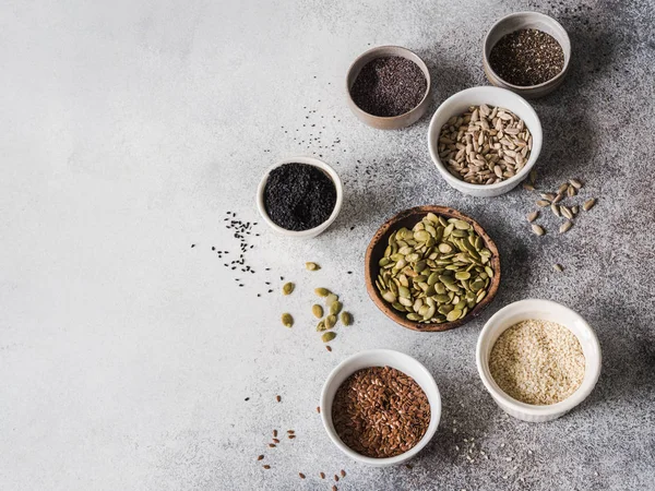 Çeşitli tohum - susam, keten tohumu, ayçiçeği çekirdeği, kabak çekirdeği, haşhaş, gri bir arka plan üzerinde kaseler chia.