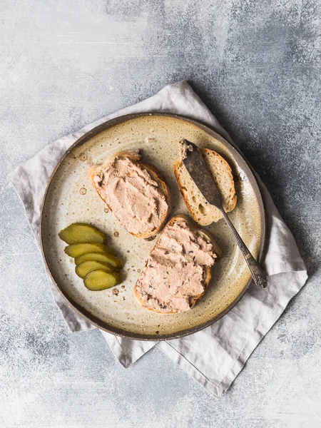 İki tost ördek ile beyaz ekmek üzerinde rillettes pate vintage plaka gri arka plan üzerinde turşu salatalık dilimleri ile ayıklar. Üstten görünüm