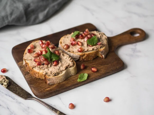 Two toasts duck with prunes rillettes pate on white bread with pomegranate seeds on a wood board on marble background. Copy space