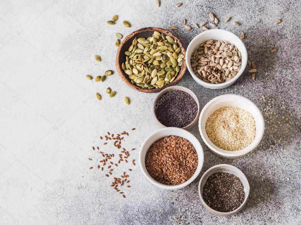 Various seeds - sesame, flax seed, sunflower seeds, pumpkin seed, poppy, chia in bowls on a gray background. Copy space.