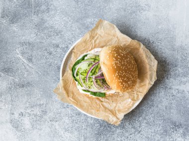 Beyaz balık fileto salatalık dilim, kırmızı soğan, taze dereotu ve ıspanak üzerinde beyaz bir plaka ile ev yapımı balık burger. kopya alanı