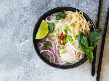 Geleneksel Vietnam çorba-pho ga tavuk ve pirinç noodle, nane ve Salantro, yeşil ve kırmızı soğan, biber, fasulye filizi ve kireç gri arka plan üzerinde siyah kase.