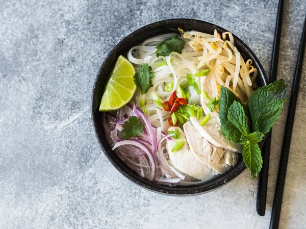 Geleneksel Vietnam çorba-pho ga tavuk ve pirinç noodle, nane ve Salantro, yeşil ve kırmızı soğan, biber, fasulye filizi ve kireç gri arka plan üzerinde siyah kase.