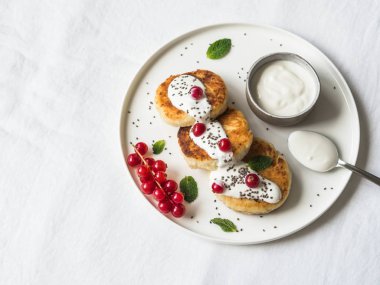 Ev yapımı peynir kek süzme peynir beyaz seramik tabak içinde nane, ekşi krema ve beyaz zemin üzerine kırmızı kuş üzümü ile servis üzerinden.