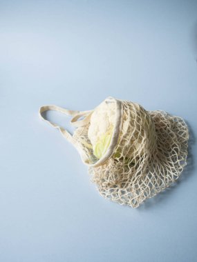 Çevre dostu bej alışveriş çantası ile mavi bir arka plan üzerinde karnabahar. Çanta sebze ile dize. Sıfır atık, hiçbir plastik kavramı.