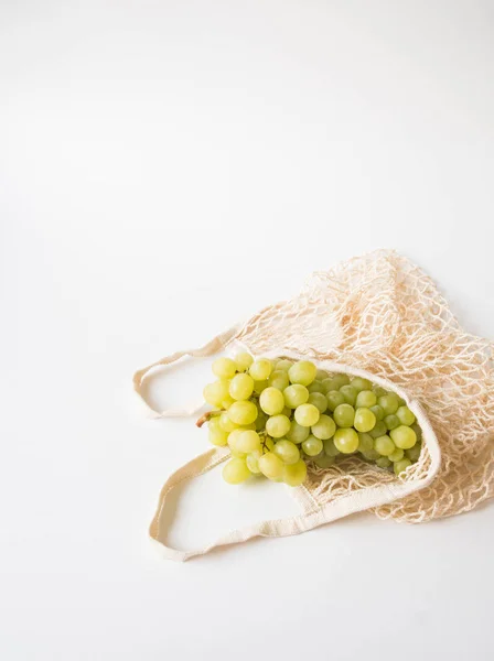 Bolso ecológico beige con uvas sobre fondo blanco. Bolsa de cuerdas con frutas. Cero residuos, sin concepto de plástico . — Foto de Stock