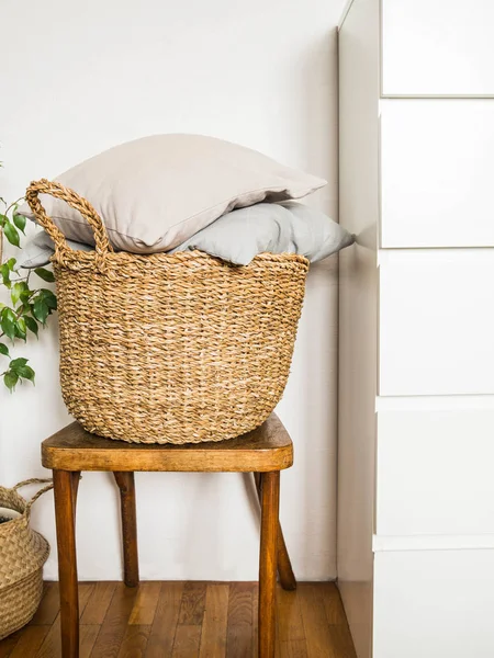 Weidenkorb mit grauen Kissen auf einem hölzernen Vintage-Stuhl vor einer weißen Wand — Stockfoto