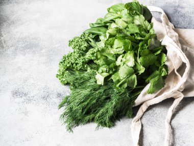 Yemek pişirmek için sağlıklı yeşil vegan maddeler. Çeşitli otlar ve keil Tekstil çanta gri arka plan üzerinde. Ürün market plastik olmadan. Kopya alanı