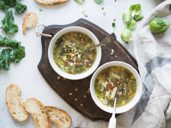 Grüne Gemüsesuppe aus Keil, Rosenkohl, Zucchini, Lauch mit verschiedenen gekeimten Samen und Rosenkohl mit Croutons auf Holzbrett. Ansicht von oben — Stockfoto