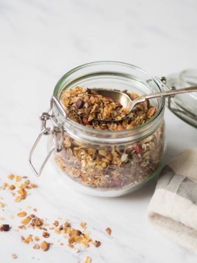 Fındık, tohumlar, goji meyveleri granola açık cam. Sağlıklı kahvaltı - mermer beyaz arka plan üzerinde bir kavanoza ev yapımı granola