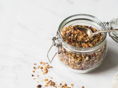 Fındık, tohumlar, goji meyveleri granola açık cam. Sağlıklı kahvaltı - mermer beyaz arka plan üzerinde bir kavanoza ev yapımı granola