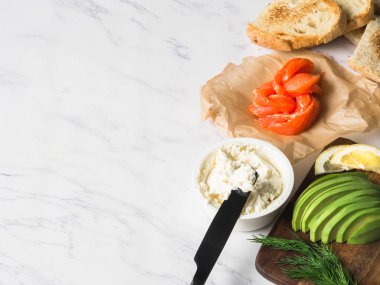 Krem peynir, somon, beyaz mermer zemin üzerinde ızgara tost üzerinde avokado ile hazırlık sandviç için malzemeler. Kopya alanı