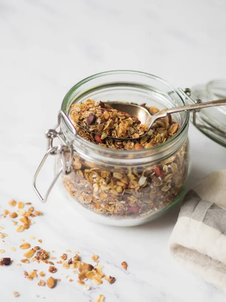 Frutos secos, semillas, bayas de goji granola en frasco de vidrio abierto. Desayuno saludable - granola casera en un frasco sobre un fondo blanco de mármol —  Fotos de Stock