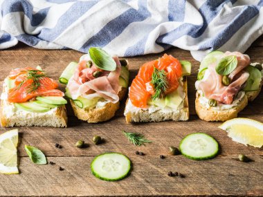 Krem peynir, somon, avokado ve krem peynir, salam, salatalığın üzerinde ahşap arka plan üzerinde ızgara tost ile sandviç.