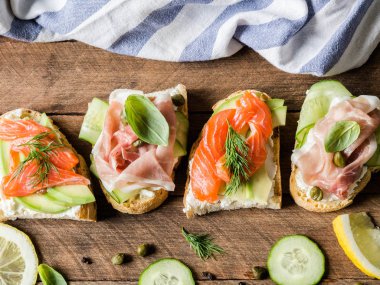Krem peynir, somon, avokado ve krem peynir, salam, salatalığın üzerinde ahşap arka plan üzerinde ızgara tost ile sandviç.