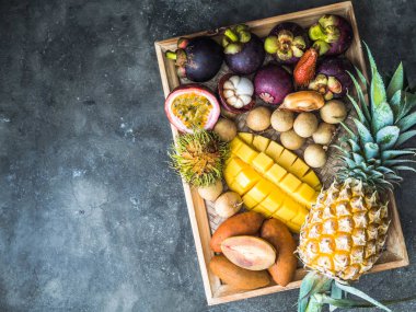 Çeşitli taze Tay meyveleri - rambutan, mango, mangosten, longan, sapodilla, tutku meyve,, ahşap bir tepsi ve gri bir arka plan üzerinde. üst görünüm
