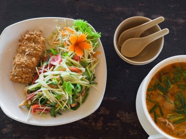 Ekşi ve baharatlı Tom Yum Goong çorbası ve yeşil mango ve bir restoranda bir masada tabakta ekmekli balık ile salata. Tay Otantik geleneksel gıda.