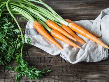 Mutfak havlusunda yeşil tepeli taze havuç kırsal ahşap arka planda.