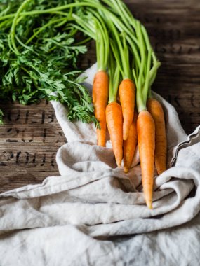 Mutfak havlusunda yeşil tepeli taze havuç kırsal ahşap arka planda.