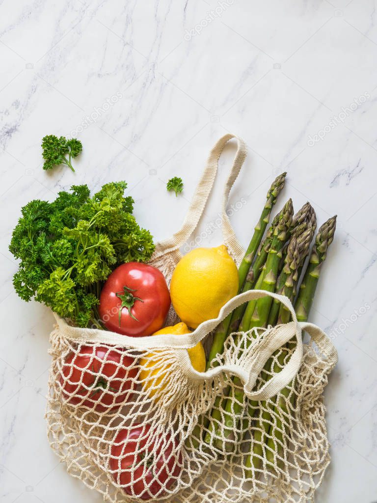 Various fresh food - vegetables and fruits in eco-friendly bag on white marble background. Vegetarian meal from the market in string bag. Zero waste concept