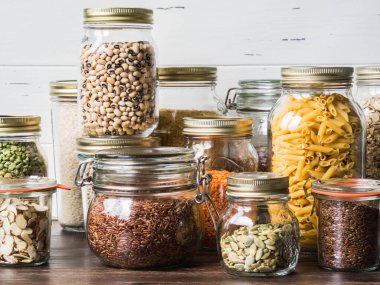 Çeşitli tahıllar ve tohumlar - bezelye bölünmüş, ayçiçeği ve kabak çekirdeği, fasulye, pirinç, makarna, yulaf ezmesi, kuskus, keten, badem, mercimek, badem dilimleri, mutfakta masada cam kavanoz bulgur